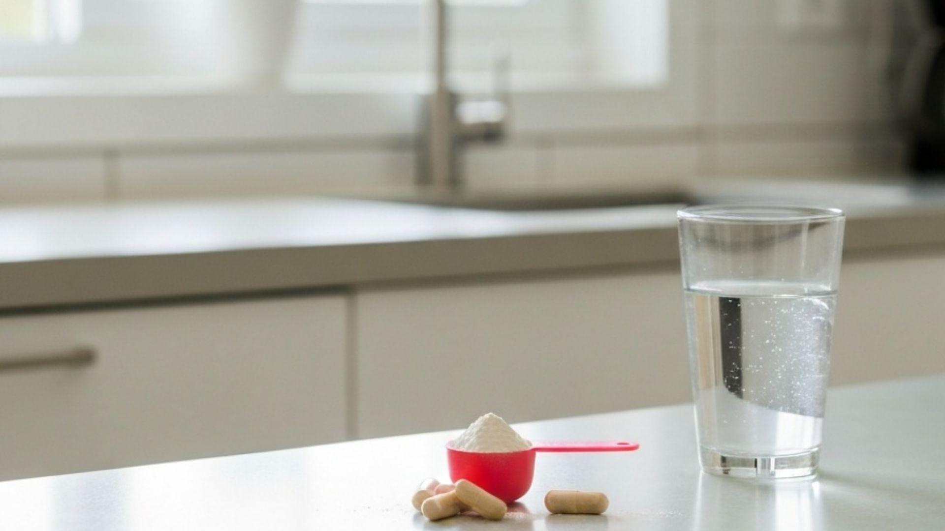 Kreatinpulver i en måleske med kapsler ved siden af et glas vand