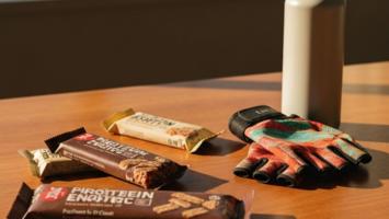 Proteinbarer og energibarer på et træbord ved siden af træningsudstyr