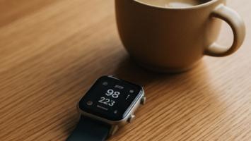Smartwatch der viser dagens skridt på et trægulvbord ved morgenkaffen