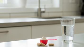Kreatinpulver i en måleske med kapsler ved siden af et glas vand